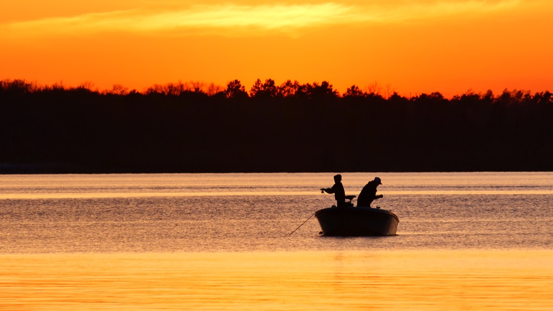 Father and son dishing on lake at sunset